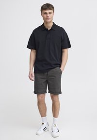 Schwarzes Poloshirt mit kurzen Ärmeln, graue Shorts und weiße Sneaker mit schwarzen Streifen. Einfaches Design und lässige Passform. Keine sichtbaren Muster.