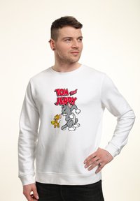 Biała bluza z nadrukiem graficznym przedstawiającym Tom'a i Jerry'ego, z wyboldowanym czerwonym napisem. Wykonana z miękkiego materiału z ściągaczami przy rękawach i u dołu.
