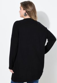 Svart långärmad tröja med ribbad halsringning och sidoklipp, med en avslappnad passform och mjuk textur, lämplig för vardagsbruk.