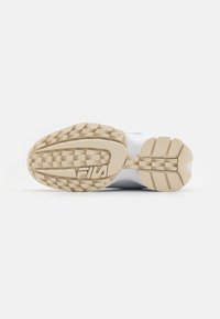 Semelle de chaussure de sport blanche avec un fond en caoutchouc beige texturé, présentant un design de grip à motifs et un logo "Fila" bien en évidence.