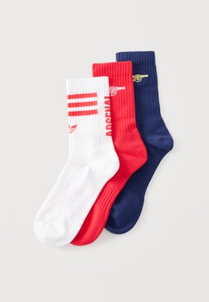 Drei gerippte Crew-Socken in Weiß mit roten Streifen, Rot mit weißem Arsenal-Schriftzug und Kanonen-Logo, und Marineblau mit gelbem Kanonen-Logo.