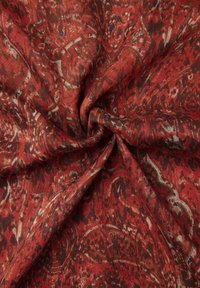 Tessuto rosso a motivo con intricate spirali e texture. Il materiale appare morbido e flessibile, con una combinazione di accenti scuri e più chiari.