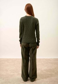 Zielony sweter w splot kabelkowy z długimi rękawami, teksturowanym wzorem i ściągaczami, połączony z szerokimi oliwkowymi spodniami z tylnymi kieszeniami.