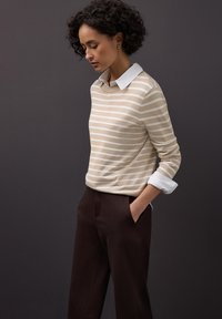 Pull rayé beige avec un col blanc, associé à un pantalon marron sur mesure. Le tissu semble doux avec une texture lisse.