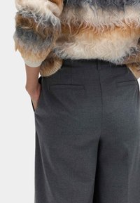 Grå skræddersyede bukser med en glat tekstur, der har to baglommer. Outfittet suppleres af en blød, multifarvet sweater.