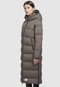 Langer gepolsterter Mantel in Taupe mit Kapuze, Reißverschluss vorne und zwei seitlichen Taschen. Das Design enthält Nähdetails zur Konturierung.