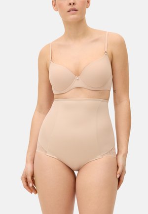 Mujer con un sujetador acolchado color nude y ropa interior moldeadora de talle alto sobre un fondo liso.