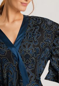 Zwarte stoffen jurk met een blauw bloemenpatroon, satijnen V-hals en brede mouwen. Het ontwerp heeft een gladde textuur en ingewikkelde details.