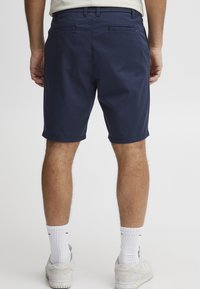 Navy blue cotton shorts with a straight cut, featuring a flat front, two back pockets, and a cuffed hem, worn with white socks and shoes.