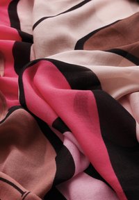 Foulard di seta multicolore caratterizzato da un tessuto morbido e fluido con motivi a onde in tonalità di rosa, nero e marrone, esposto in pieghe.