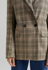 Dwuczęściowa marynarka w kratę w odcieniach brązu i beżu, z czarnymi guzikami, dwoma przednimi kieszeniami oraz długimi rękawami w luźnym kroju.