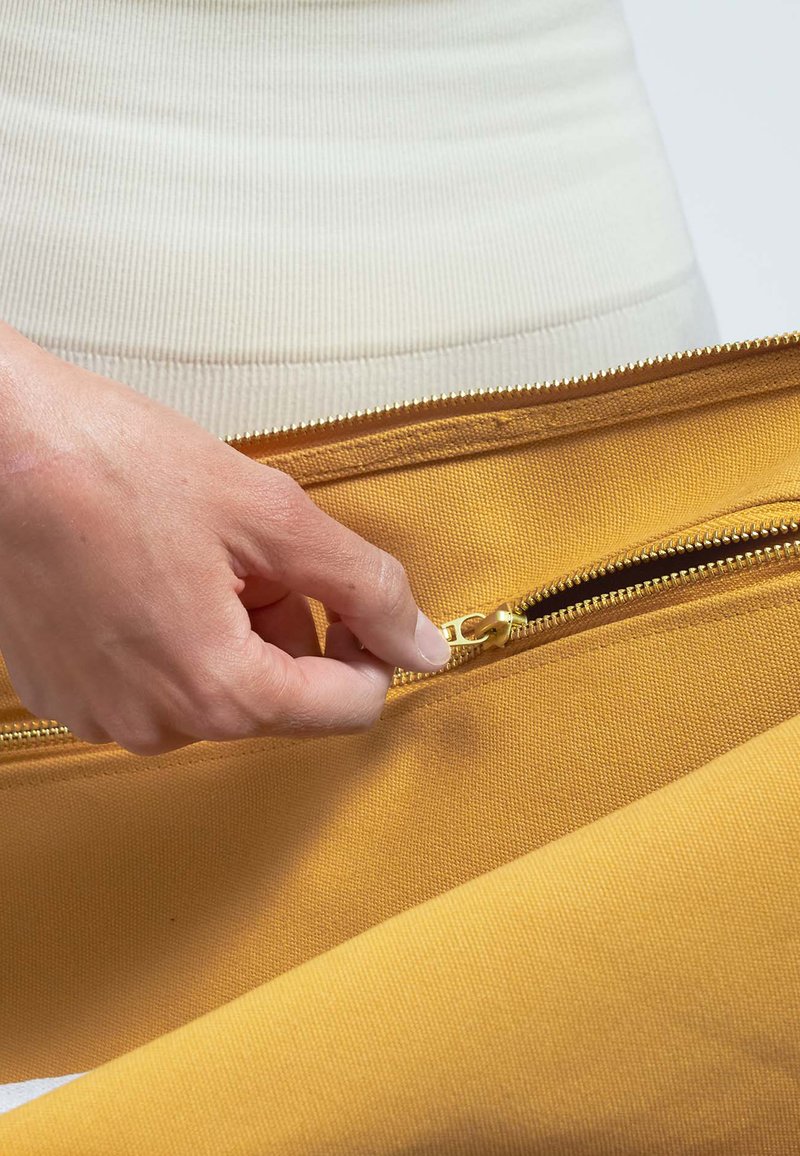 Cierre dorado siendo tirado de una bolsa amarilla brillante hecha de un tejido resistente, que muestra una superficie texturizada y un diseño limpio.