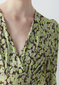 Robe enveloppante à motifs marron et verts avec un décolleté en V profond, une texture douce et des manches plissées avec un accent de bouton à la taille.