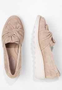 Bottes en daim beige à enfiler avec un détail de nœud torsadé sur le dessus, semelle en caoutchouc blanche épaisse, présentées en vue de dessus et de côté sur fond blanc.