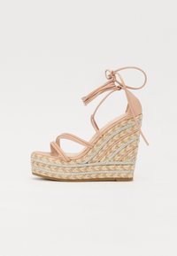 Sandaler med kilehæl med en vevd jute-bunn, beige syntetiske stropper og flettede sølvdetaljer. Har en høy hæl med knytelukking.