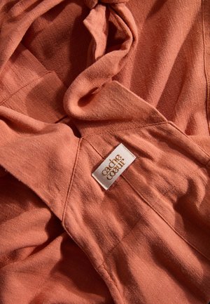 Baumwollstoff in gedämpftem Korallenfarbton, mit weicher Textur und fließendem Design, versehen mit einem sichtbaren Etikett, das "each coeur" beschriftet ist.