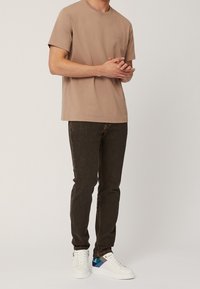 Brun bomulls-t-shirt med korta ärmar, i kombination med mörkbruna slim-fit jeans och vita sneakers med blå och grå detaljer.