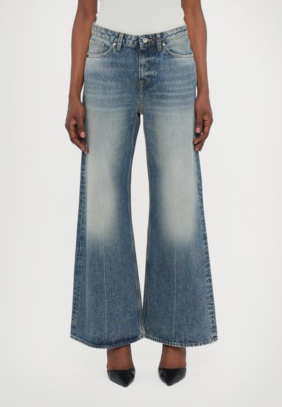 Jeans din denim cu picioare largi, de culoare albastru deschis, cu decolorare, design cu cinci buzunare, închidere cu nasture și tiv ușor desfăcut. Poartă cu pantofi cu toc negri.