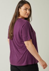 Lila kortärmad t-shirt i en mjuk bomullsblandning, med en avslappnad passform och sidoflikar för komfort. Enkel och slät textur.