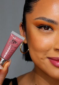 Producto de labios Colorfix mate en un tubo, tono rosa suave con tapa plateada metálica, sostenido por una persona con una piel suave y radiante.
