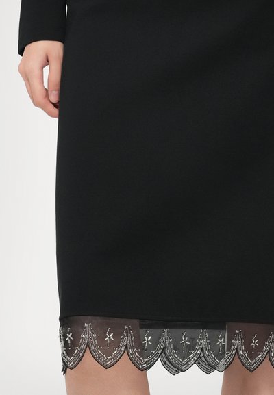 Fekete ruha áttetsző szegéllyel, hullámos éllel és ezüst hímzéssel, amely kontrasztos textúrát alkot. Simább anyag a szegély felett.