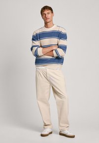 Ribadega kootud sviiter beeži ja sinise värviga, kombineeritud koorevalgete pükste ja valgete tossudega. Omab soonikuid mansetid ja lõtv sobivus.