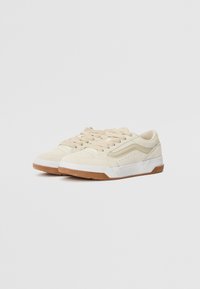 Beige sneakers with a suede upper, white accents, and a gum rubber sole. Features laces, subtle perforations, and a low-profile design.