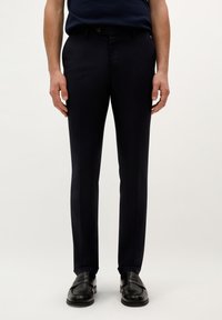 Pantalones de marina con una textura suave, que presentan un corte slim, trabillas para cinturón y un único bolsillo frontal, combinados con zapatos de vestir negros.