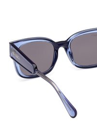 Ochelari de soare bleumarin cu un design geometric. Lentile întunecate, ramă transparentă și un logo argintiu pe lateral. Formă elegantă și unghiulară.