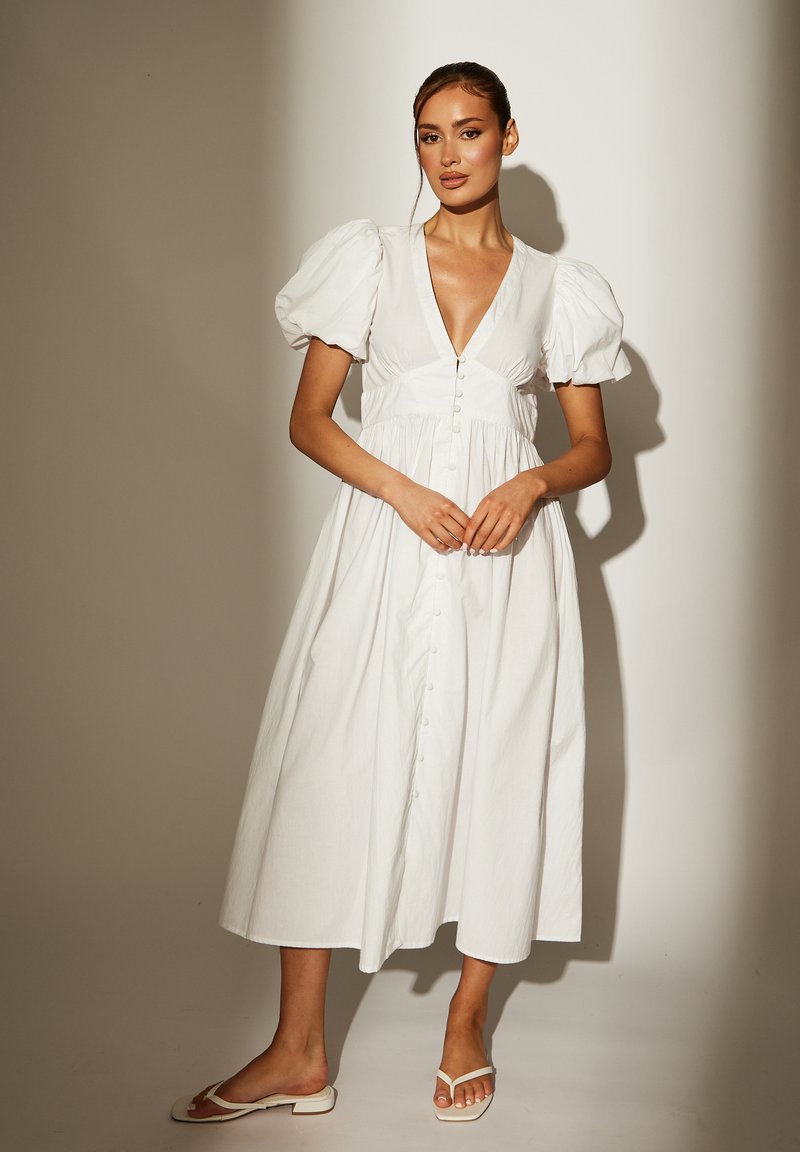 Weißes, knielanges Kleid mit Puffärmeln, tiefem V-Ausschnitt und durchgehender Knopfleiste. Hergestellt aus einem leichten Stoff; glatte Textur und fließendes Design.