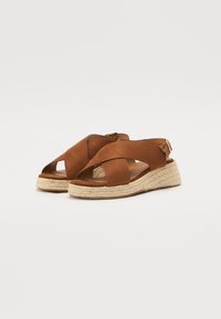Brown suede sandals with an espadrille wedge sole, featuring crossed straps and an ankle buckle detail. Textured material enhances grip.