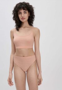 Perzikkleurige crop top met dunne straps en bijpassende high-waisted panties van soepel materiaal, met een naadloos ontwerp en subtiele rek.