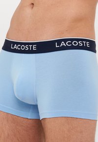 Boxer ajustados de algodón en color azul claro con una banda en la cintura de color navy que presenta la inscripción "LACOSTE". Textura suave y diseño ceñido.
