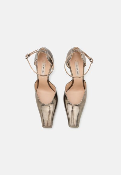 Tacones altos metálicos plateados con correa al tobillo, diseño de punta afilada y textura suave. Plantilla en un tono beige claro.