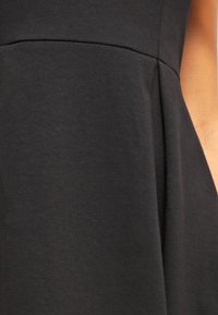 Svart bomullsklänning med en åtsittande bodice och en svävande kjol. Slät yta, minimal detaljering och subtila veck vid midjan.