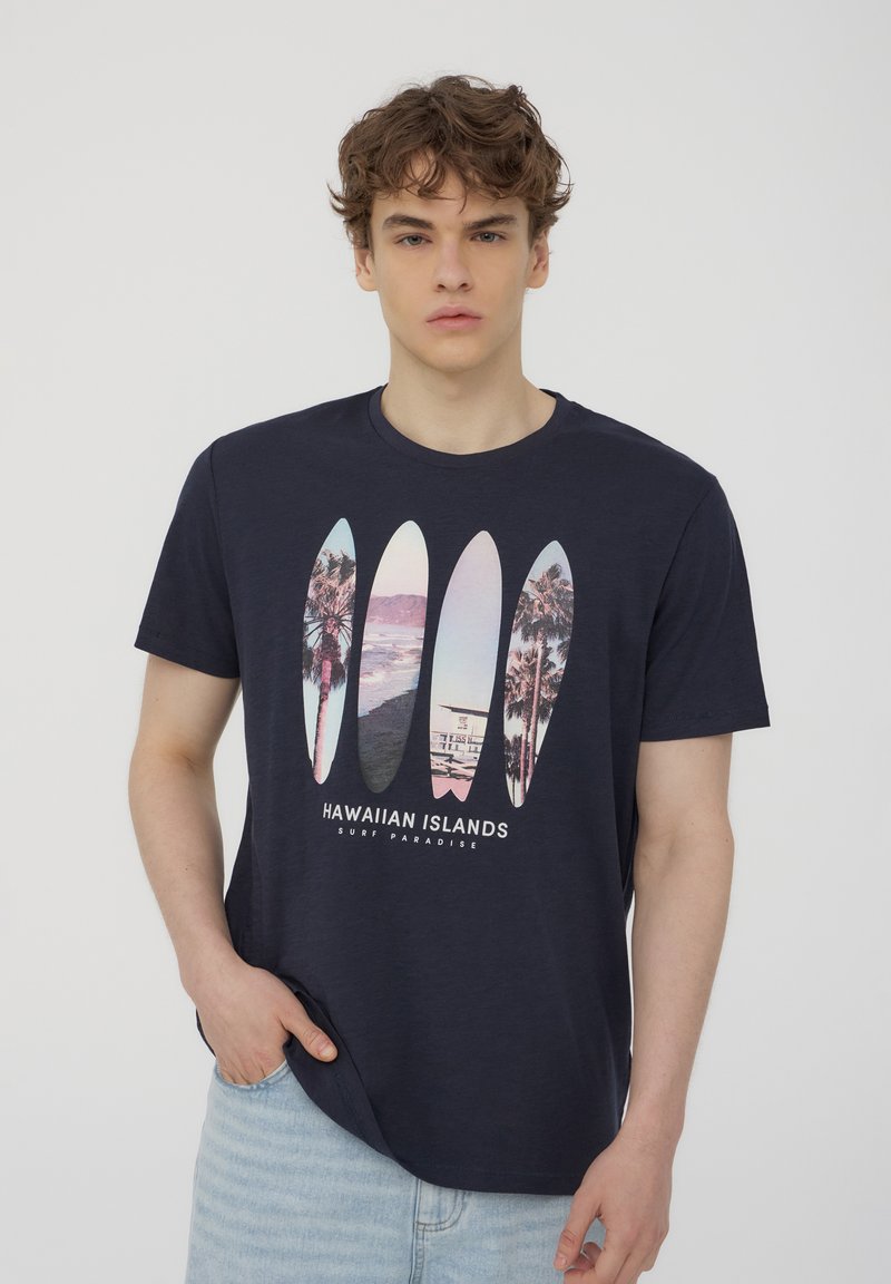 T-shirt in cotone blu navy con una grafica di cinque tavole da surf, che include palme e immagini costiere, con il testo "ISOLE HAWAIANE" sotto.