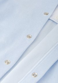 Cárdigan de punto azul claro con botones a presión plateados, que muestra una textura suave y un diseño en capas, cuenta con un cuello y puños acanalados.