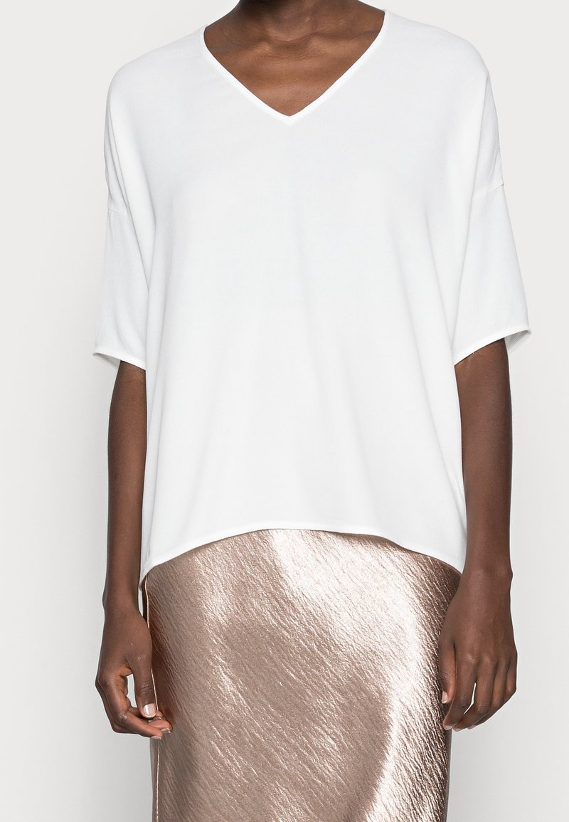 Hvid v-neck top med korte ærmer, lavet af et glat materiale, parret med en blank, roseguld, knælang nederdel.