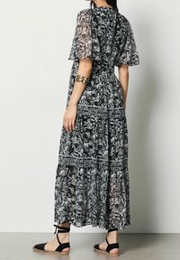 Svartvit blommig maxiklänning med korta svängande ärmar, lagerdesign och åtdragen midja, tillsammans med svarta sandaler.
