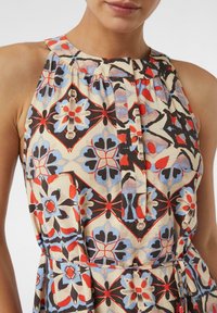 Ärmelloses, mehrfarbiges Kleid mit floralen Mustern in Rot, Blau und Schwarz. Der Stoff ist leicht, mit einer taillierten Taille und Knopfdetails.