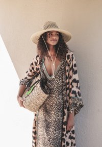 Robe maxi à imprimé léopard avec un décolleté en V profond, accentuée par des coutures turquoise. Chapeau en paille à large bord et sac en osier avec quincaillerie noire.