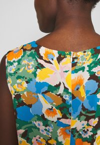 Top sin mangas con estampado floral que presenta patrones vibrantes en azul, naranja, verde y rosa. Incluye una cremallera en la parte posterior y una textura de tela suave.