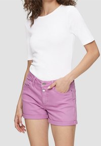 Pantalones cortos de mezclilla morados con dobladillos enrollados, que cuentan con bolsillos frontales, cierre de botón de metal y una camiseta blanca ajustada y lisa.