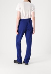 Blå mjukisbyxor i en avslappnad passform med elastisk midja, kombinerade med en enkel vit t-shirt. Texturen verkar mjuk med en slät yta.