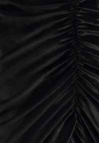 Tissu en velours noir avec fronces verticales créant des plis texturés et une légère brillance.