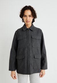 Giacca grigia in misto lana con colletto, due tasche sul petto e due tasche laterali, dallo stile rilassato e dalla texture morbida.
