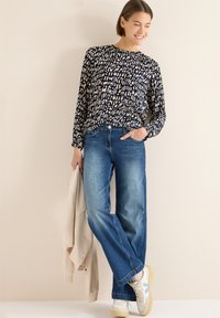 Laivastonsininen, kuvioitu pitkähihainen paita, jossa on kermanväriset yksityiskohdat, yhdistetty vaaleansinisiin leveälahkeisiin farkkuihin ja beigeen takkiin, jonka kanssa valkoiset lenkkarit.