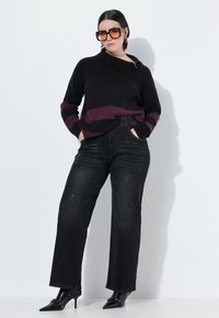 Maglione nero con zip e striscia bordeaux, abbinato a jeans a gamba larga neri e testurizzati. Il modello indossa occhiali da sole oversize e stivali a punta.