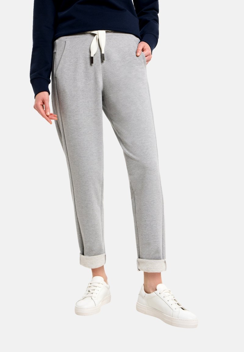 Graue Jogginghose mit lockerem Schnitt, gekrempelten Säumen, Kordelzug in der Taille, Fronttaschen; getragen mit weißen Sneakern. Glatte Textur.