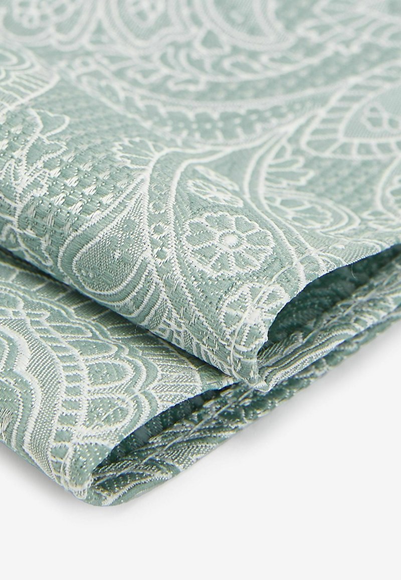 Grøn paisley-mønsteret stof med hvide, indviklede designs, der har en tekstureret overflade og sammenfoldede kanter, som viser detaljeret håndværk.